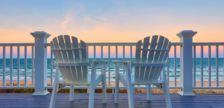 two white chairs on a patio overlooking a beach sunset