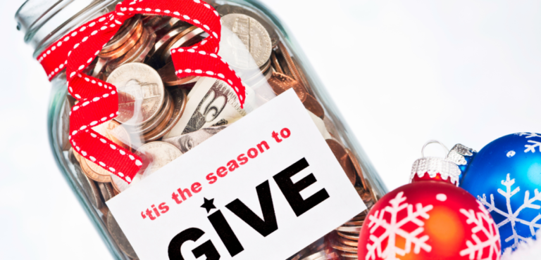 A jar with money that says "Tis the Season to GIVE" and a red ribbon around it and a red and blue Christmas tree ball ornament paying next to it