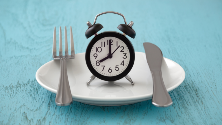 A blue background. In the middle is a plate with a clock on it. On the left is a fork and on the right is a knife.