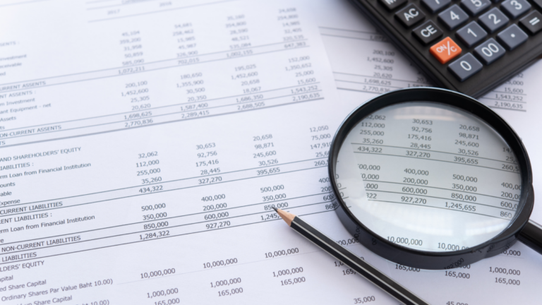 An image of a financial statement with a magnifying glass, calculator, and pencil on top of it.