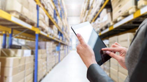 A close-up of a woman holding an ipad in a warehouse