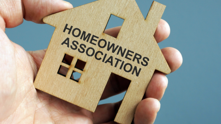 A hand holding a cutout of a house that has the words "homeowners association" printed on it.