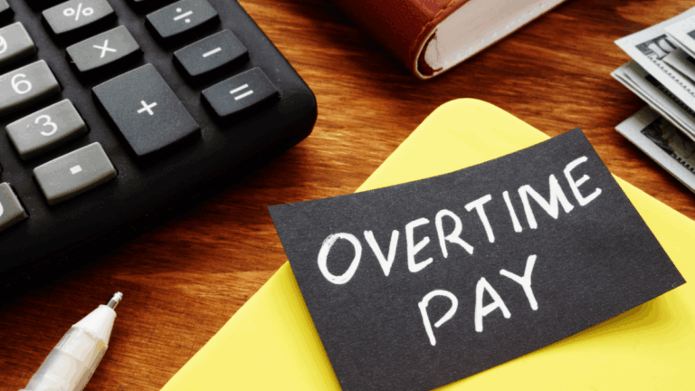 Top of a desk with a calculator, some folders, and a note that says "overtime pay"