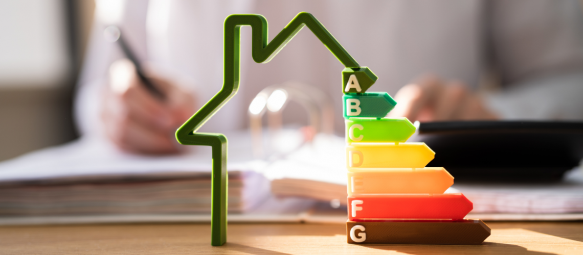 In the background, someone is working at a desk. In the foreground there is a model of an energy efficient home with a rating scale on it.