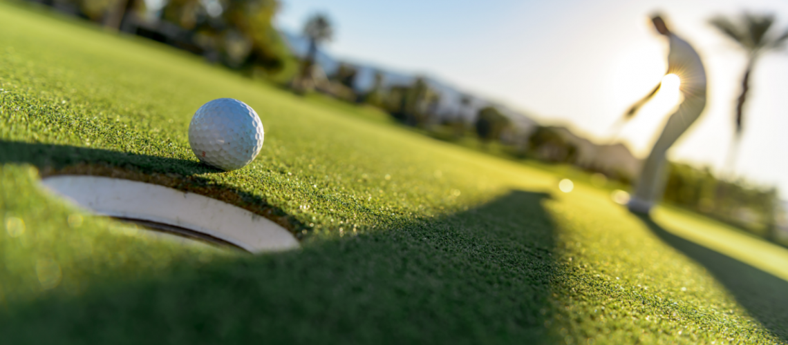 An image of a golfer on a golf course with a ball about to go into the hole.
