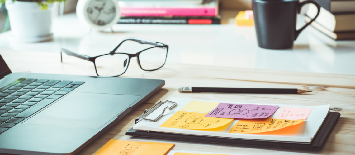 A desktop showing a laptop, sticky notes, a clock, and a coffee mug