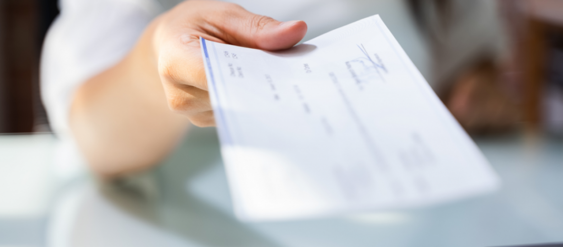 a photo of a woman's arm extending towards the camera holding a check which is all blurred out.