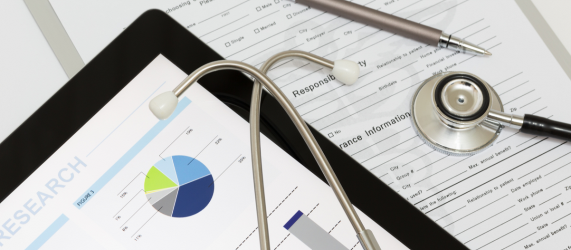 A desktop zoom-in with a stethescope, an ipad showing financials and a patient form