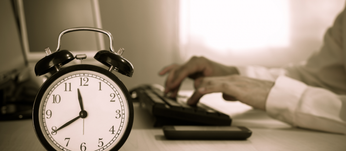 A grey photo of a clock and behind it is someone typing on a keyboard