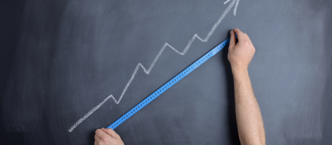 A chalkboard with a jagged arrow drawn that is pointing up. Two hands hold a blue measuring tape to see how long it is