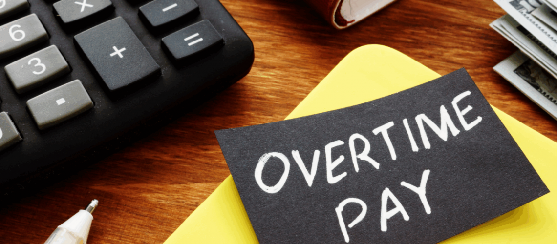 Top of a desk with a calculator, some folders, and a note that says "overtime pay"