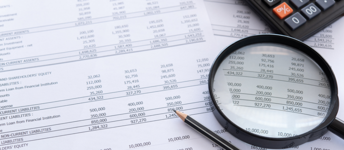 An image of a financial statement with a magnifying glass, calculator, and pencil on top of it.