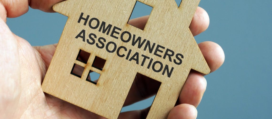A hand holding a cutout of a house that has the words "homeowners association" printed on it.