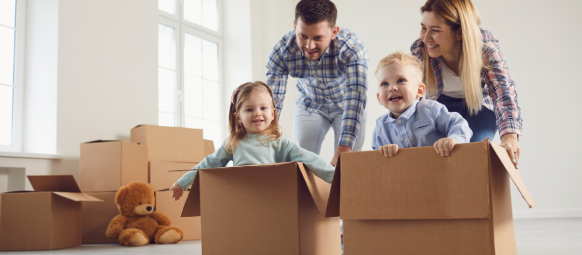 a mother and father playing with their children by pushing them around the house in moving boxes
