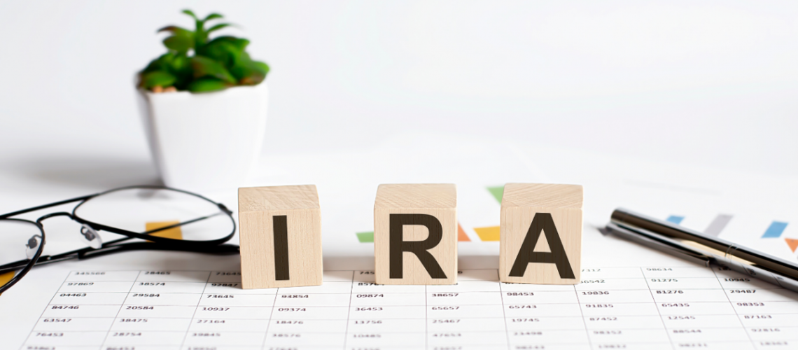 Paper with numbers on a desk, glasses to the left, a plant in the background, a pen to the right and three wooden blocks in the middle with the letters "I" "R" "A"