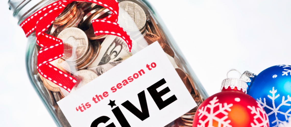 A jar with money that says "Tis the Season to GIVE" and a red ribbon around it and a red and blue Christmas tree ball ornament paying next to it